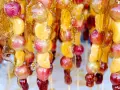 Spiedini di frutta caramellata con acqua e zucchero, con uva e spicchi d'arancia lucidi e dorati.