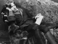 Oscar Wilde, w futrzanym płaszczu, z książką w dłoni, w pozie sugerującej refleksję nad swoimi sztukami.
