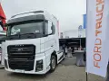 Biały Ford F-MAX prezentuje się na wystawie, obok banerów z logo Ford Trucks.