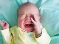 Ein **baby weinen** auf einem türkisfarbenen Tuch, mit geschlossenen Augen und einer Hand vor dem Gesicht.
