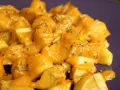 Patatas bravas crujientes cubiertas con una salsa naranja cremosa y hierbas picadas.