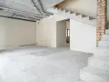 Wnętrze w stanie deweloperskim: betonowe schody, nieotynkowane ściany, widoczne instalacje i przewody.