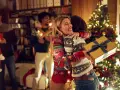 Zwei Frauen umarmen sich vor einem Weihnachtsbaum, eine hält ein Geschenk. Eine Familie feiert Weihnachten, eine der vielen schönen weihnachtstraditionen deutschland.