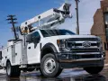 Biały Ford F650 z podnośnikiem koszowym gotowy do pracy przy liniach energetycznych.