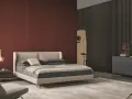 Habitación moderna con pared texturizada en rojo terracota, cama beige y cómoda gris. Inspírate para como pintar una habitacion.