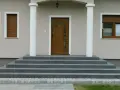 Elegancka, zewnętrzna klatka schodowa w domu jednorodzinnym prowadzi do brązowych drzwi z witrażem.