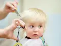 Ein kleines blondes Kind bekommt die Haare geschnitten. Die Schere nähert sich vorsichtig den feinen Strähnen.
