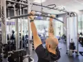 Man med tatueringar utför enarms latsdrag på ett gym.