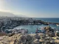 Malowniczy port na Cyprze w listopadzie. Wiele łodzi i jachtów cumuje w zatoce, a w tle widać miasto i góry.