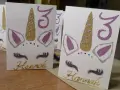 Glitzernde Einhorn-Einladungen zum 3. Geburtstag basteln. Hannahs Name ist in Goldbuchstaben geschrieben.