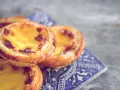 Ein Stapel goldbrauner, karamellisierter Pastel de Nata auf einer blauen Kachel.