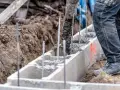 Betoniarka wylewa beton do szalunku. Pracownik w czarnych spodniach nadzoruje proces, który jest kluczowy, by wiedzieć, jak obliczyć kubik betonu.