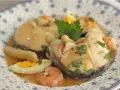 Merluza a la vasca con gambas, huevo duro y perejil, servida en un plato con diseño floral.