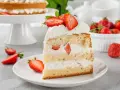 Puszysty biszkopt przełożony kremową masą z mascarpone i kawałkami truskawek, udekorowany świeżymi owocami.