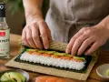 Ręce zwijają sushi z łososiem i awokado. Obok butelka octu ryżowego "Tokyoto" - idealna zaprawa do sushi na 500g ryżu.