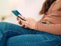 Kobieta w dżinsach i bluzce z długim rękawem trzyma telefon. To może być obraz skutków zbyt długiego korzystania z telefonu.