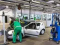 Un meccanico in tuta verde controlla un'auto argentata in un'officina, forse per un controllo secondo l'articolo 80 del codice della strada.
