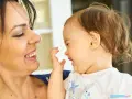 Uśmiechnięta mama patrzy na swoje dziecko, które bawi się i śmieje, wyciągając rączkę.