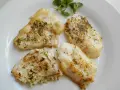 Cuatro trozos de pescado blanco rosada a la plancha, sazonados con hierbas, servidos en un plato blanco con una ramita de perejil.