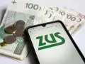 Złotówki i monety obok telefonu z logo ZUS. Może to być związane z wnioskiem o zasiłek opiekuńczy.