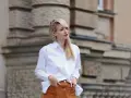 Mujer con falda de gamuza y camisa blanca, posando con las manos en los bolsillos.