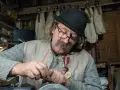 Piotr Majerczyk, z siwym dymem w tle, skupiony na pracy, w kapeluszu i z medalami na piersi.