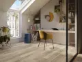 Luminoso studio mansardato con scrivania, sedia gialla e un elegante **pavimento polvere di pietra** che riflette la luce naturale.