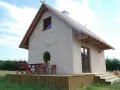 Mały domek z gliny na działce budowlanej, z drewnianym tarasem i meblami ogrodowymi.