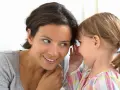 Dziecko szepcze mamie do ucha. Czasem powtarzanie słów, jak w palilalia u dzieci, może być etapem rozwoju mowy.