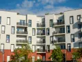 Immeuble moderne aux balcons noirs, un **idéal de la loge** avec ses façades blanches et sa base rouge. Ciel bleu et nuages.