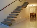 Escaleras rústicas modernas de hormigón flotante con pasamanos de madera. Un camino de guijarros blancos bordea la base.