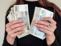 Dłonie z paznokciami w pastelowym różu trzymają pliki polskich banknotów 100 i 50 zł. To może być nagroda jubileuszowa.