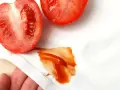 Plama z pomidora na białej tkaninie, obok przekrojonych pomidorów.