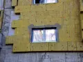 Pannelli di lana di roccia per cappotto termico spessore, fissati con tasselli rossi su un edificio in costruzione.