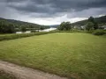 Łąka nad rzeką, domy w oddali. Chmury zapowiadają deszcz, budząc obawy o zagrożenie powodziowe.