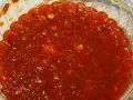 Gęsty, czerwony sos sambal w przezroczystym pojemniku, z widocznymi kawałkami papryczek chili i przypraw.