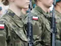 Żołnierze w mundurach z polskimi flagami, gotowi do marszu. Słychać przyśpiewki wojskowe.