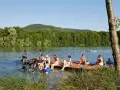 Menschen genießen einen sonnigen Tag am Baggersee Happurg. Sie sitzen auf einem Holzsteg, schwimmen und entspannen sich im Wasser.