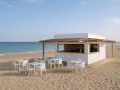 Un chiringuito moderno en la playa, listo para servir. Mesas y sillas blancas esperan a los clientes.