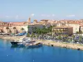 Malowniczy port na wyspie z Ajaccio, z luksusowymi jachtami i palmami, w tle kolorowe kamienice i wieża kościelna.