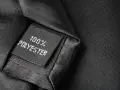 Czarna metka z napisem "100% POLYESTER" na tle eleganckiego materiału. Czy poliester to dobry materiał?