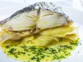 Merluza al horno con patatas, jugosa y dorada, servida sobre patatas tiernas y bañada en aceite de oliva con perejil picado.