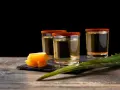 Trzy kieliszki z tequila i mezcal, ozdobione solą chili, obok pomarańczy i liścia agawy.