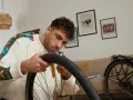 Mężczyzna w kolorowym swetrze naprawia rower, wyjmując dętkę.
