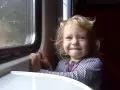 Uśmiechnięta dziewczynka z blond włosami patrzy przez okno pociągu, zastanawiając się, gdzie pociągiem z Krakowa zabierze ją podróż.