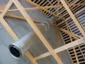 Installation d'un tubage cheminée en métal dans une charpente en bois. Le conduit traverse un mur en parpaings.