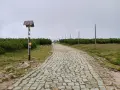 Kamienna ścieżka w górach, pośród kosodrzewin. Na pierwszym planie drewniany słup z drogowskazami, przypominający spaloną strażnicę.