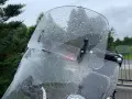 Przednia szyba motocykla pokryta kroplami deszczu, z widocznymi mocowaniami.
