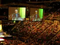 Große Menschenmenge in einer Arena, die einer Predigt von der **United Church of Christ** auf einer Leinwand folgt.