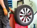 Meccanico con guanti arancioni controlla la vibrazione auto semiasse su una macchina bilanciatrice.
